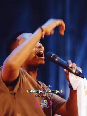 The image showcases a man singing into a microphone with his arm raised. He's wearing a brown short-sleeved shirt. The background is dark, possibly a stage. Text overlay is present with design elements. Overall, it's a performance shot.
