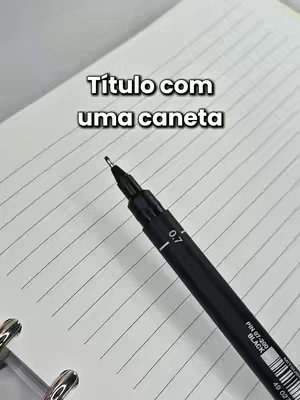 A close-up shot showcases a black pen on a white, lined notebook page. The pen is angled, with its tip positioned towards the viewer. Overlayed text in a sans-serif font reads 'Título com uma caneta'. The composition is simple and sharp, emphasizing details and the act of writing.