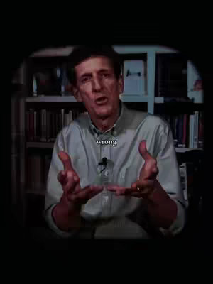 A man with short dark hair, wearing a light blue collared shirt, stands in front of a backdrop of books. He is speaking while gesturing with his hands. The word 'wrong' is overlaid on the image in a simple white font.