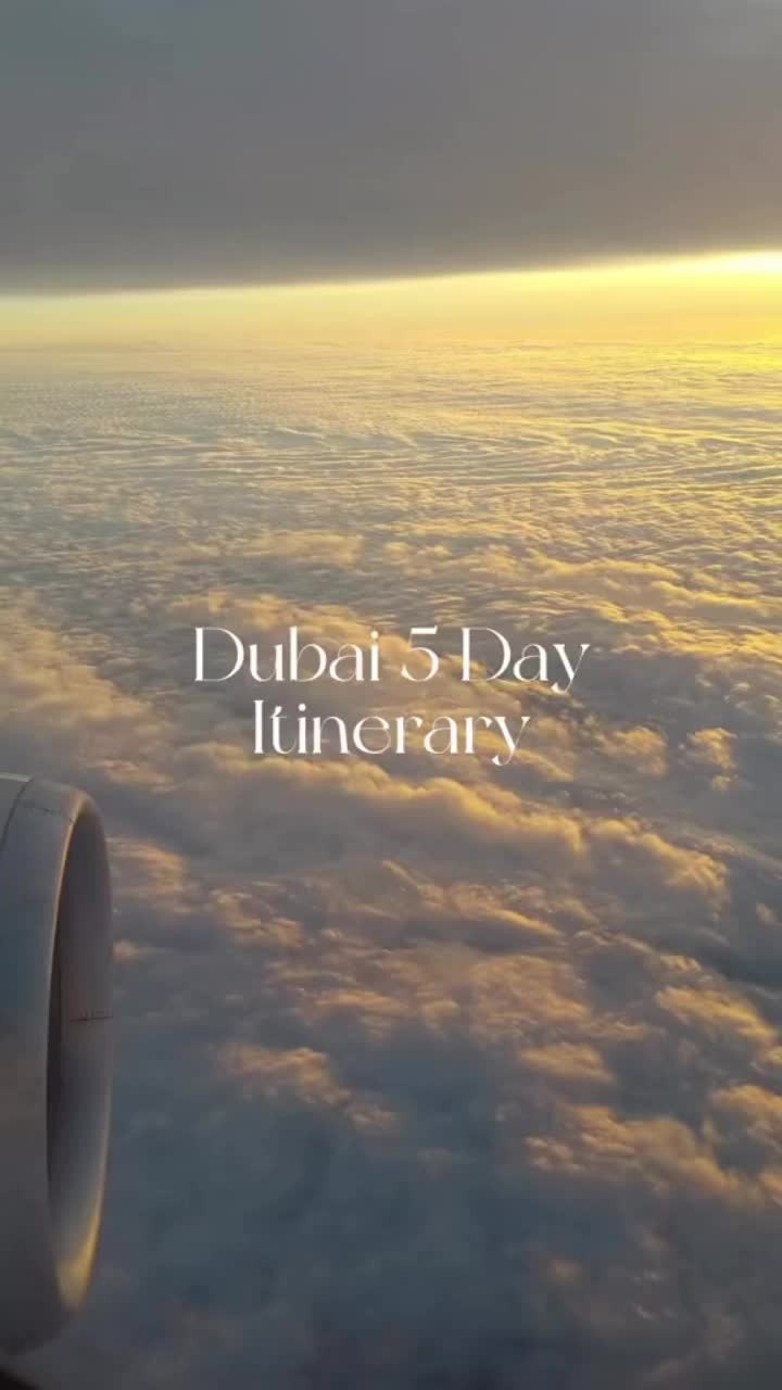 An aerial view looking through an airplane window. The image captures a sea of clouds at sunset, with hues of gold and orange illuminating the lower portion of the frame and a darker, gray tint on the top portion. The engine of the plane is visible on the left side.