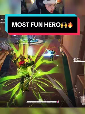 The cover image features a first-person perspective of a video game scene. A character with green energy effects is in the foreground, while other characters are visible in the background. The top of the image shows a person wearing a black beanie and headphones, likely the gamer. A text overlay with a red and blue background reads "MOST FUN HERO". The game environment appears to be a futuristic or stylized arena.