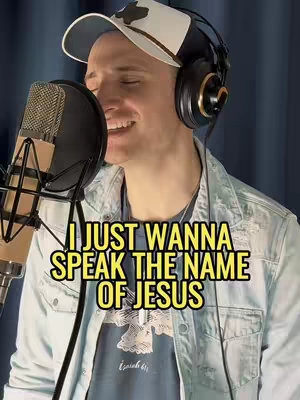 A man wearing a cap and headphones is singing into a microphone. A text overlay reads 'I JUST WANNA SPEAK THE NAME OF JESUS.' The image has a slightly warm color tone.