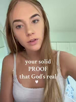 A young woman with long blonde hair is the central focus, captured in a close-up shot. She wears a white tank top, against a subtly blurred background, possibly indoors. Text overlayed on the image reads in a sans-serif font, 'your solid PROOF that God's real' with a heart symbol beneath the text.