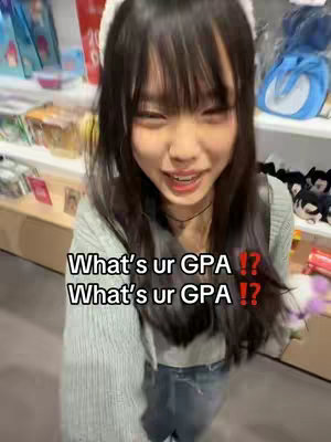 A young Asian woman with long, dark hair and bangs is smiling at the camera. She is wearing a light-colored sweater and stands in a shop or store, as indicated by the background.