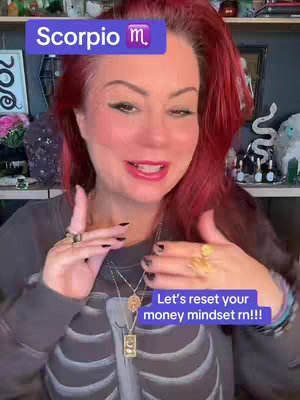 A medium shot shows a woman with red hair, wearing a gray skeleton-themed sweatshirt and multiple necklaces, talking directly to the camera. Overlay text boxes are present. The background is blurred, but other objects can be seen.
