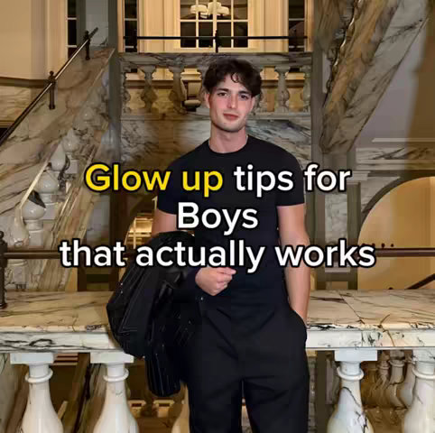 A young man in a black t-shirt and black pants poses on a marble staircase, holding a black jacket over his arm. The background includes ornate architectural details and a window. Yellow text is overlaid on the image.