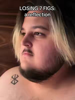 A medium shot features a man with light-colored hair on top and darker hair on the sides, looking slightly off-camera to his left. The text overlay reads “LOSING 7 FIGS: a reflection”. He has a mustache and beard. There is a tattoo on his left shoulder, and the background is dark, possibly a wall or headboard.