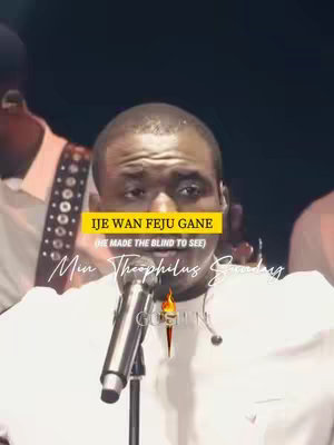 The cover image shows a man holding a microphone, centered on the upper body with additional people out of focus to the sides, set against a dark concert stage background. The man is the primary focus, dressed in a white shirt, with text overlays positioned above and below to identify the song and artist.