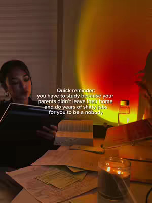 A dimly lit room with a woman sitting at a desk. She is leaning over some papers, reading or studying. A candle is burning in the foreground.  A sunset lamp casts a warm light on the wall behind her. Text in a white box overlays her papers, describing the reasons to study..