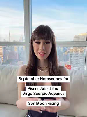 A young woman is centered in the frame, set against a large window overlooking a cityscape. She's smiling at the camera, wearing two delicate gold necklaces and her hair is styled with bangs. Overlayed on her are white rectangles with text, which are the title and names of zodiac signs.