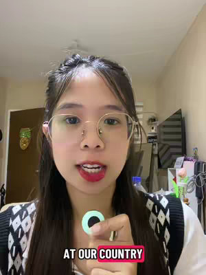 The image is a selfie-style video shot with the creator in the foreground. The creator has fair skin, glasses and dark hair with a subtle face expression. She is holding a round object. Behind her is a setting with neutral colors and a slightly out-of-focus background. The text is in a red rectangle above the word country.
