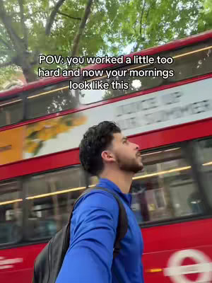 A man in a blue shirt stands on a street, facing upward. A red double-decker bus with white text is passing him on the right side. Trees and sky are visible at the top, with the text overlayed on the top left.