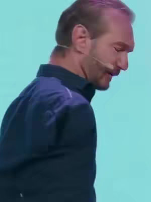 A man is shown in profile, speaking into a lavalier microphone. He is wearing a dark blue shirt against a light blue background.