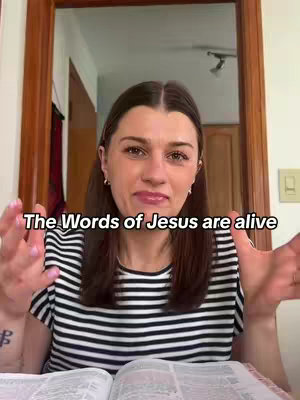 A woman with brown hair and a striped shirt is speaking to the camera. She's in a room with a doorway behind her. The overlay text in the image says: "The Words of Jesus are alive." She is holding a bible.