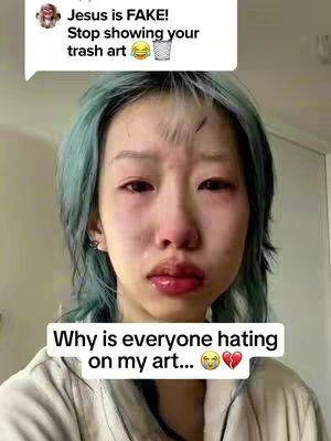 The cover image is a selfie of a young woman with teal-colored hair crying, showing a close-up of her face. Her eyes are red and filled with tears, and she has a distressed facial expression. Below her face, a text overlay reads, "Why is everyone hating on my art…😥💔". Above her is a comment bubble visible that says, "Jesus is FAKE! Stop showing your trash art" This composition suggests a theme of emotional distress, possibly related to criticism.