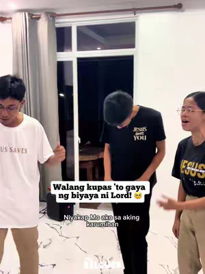 The cover image shows three individuals standing in what appears to be a home setting. The person on the left has short, dark hair and wears glasses, a white t-shirt with the words "JESUS SAVES" on it, and khaki pants. The central figure, with their back to the camera, dons a black t-shirt that says "JESUS LOVES YOU" and also wears dark pants. On the right, another person wearing glasses and a black t-shirt that says "JESUS" is visible. The text overlay on the image includes a message in Filipino, set against a semi-transparent black block in the center, and white text.