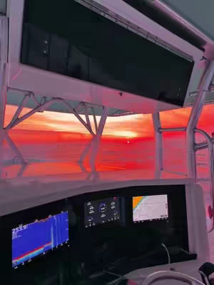 A view from inside a boat looking out at a vivid sunset. The interior of the boat is visible, with gauges and dashboards in the foreground. The sky is a vibrant gradient of reds and oranges.