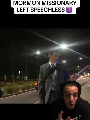 The image is a vertical video still, showcasing a split-screen composition. The upper section features a nighttime outdoor scene with focused lighting, possibly streetlights or headlights, illuminating a man in a suit walking along a road. The bottom portion displays a person's face, likely the content creator, with a concerned expression and hand gestures. The creator is in a black hoodie, and the lighting and focus suggest a close-up recording. The text overlay reads "MORMON MISSIONARY LEFT SPEECHLESS" and a cross symbol.
