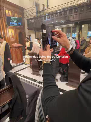 A person is filming inside a church, holding a phone toward the service with other people in attendance. The main subject is holding the phone in front of themselves, toward the service. The text overlay reads not my dad being the og Christian content creator. The scene is filled with various people and religious figures, the space has high ceilings and is illuminated from within.