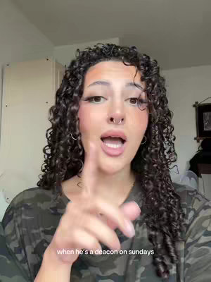 A woman with curly hair is pointing her finger and looking at the camera. She has makeup on, an open mouth, and is wearing a camo shirt. Text is added to the bottom of the image.