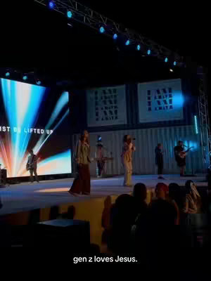 A stage with several performers, a large screen displaying abstract visuals, and an audience visible in the foreground. The lighting is dramatic.  The text overlay says "gen z loves Jesus."