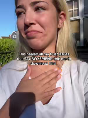 A woman with blonde hair, wearing a white shirt, stands outdoors against a backdrop of greenery and a building. She looks slightly off-camera, with a hand placed over her chest. Text overlayed on the image conveys a message about trust issues and a boyfriend.