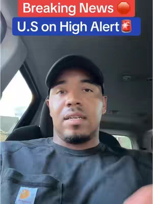 A man in a black Carhartt t-shirt and a baseball cap is filming inside of a car. The top of the video has text that reads: "Breaking News" and "U.S. on High Alert".