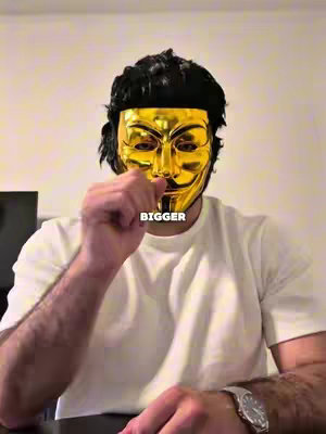 A person wearing a gold Guy Fawkes mask stands with their right hand raised near their face. The hook text "BIGGER" is overlaid on the image.