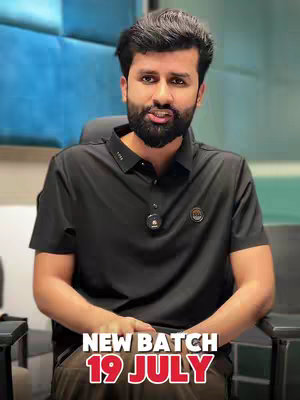 A man with a beard is centered in the frame, facing the camera and speaking. Text overlayed at the bottom reads "NEW BATCH 19 JULY" in a bold, red font. The man is wearing a black polo shirt, and a lavalier microphone is attached to his shirt. The background consists of a blue and gray paneled wall. The lighting in the shot is bright and even, illuminating the man's face and the text overlay.