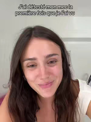 A woman with long, dark hair is looking at the camera with a soft expression. Overlayed text in a sans-serif font reads "J'ai détesté mon mec la première fois que je l'ai vu." The background appears to be a light interior setting.