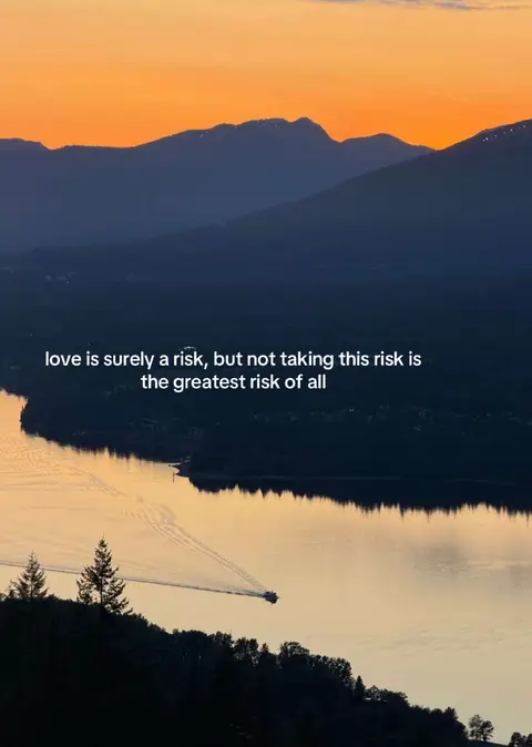 An image capturing a tranquil landscape with a lake or sea in the foreground. The sky transitions from a warm orange at the horizon to a darker blue above, suggesting either sunrise or sunset. The text overlayed on the image includes a quote about love and risk. A body of water reflects the sky's colors, and the distant silhouettes of mountains add depth. A boat is visible on the water.