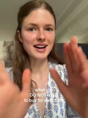 A young woman is centered in a close-up shot, with her arms extended towards the camera on either side. The background is neutral. Text overlayed on the image reads, 'what you DO NOT NEED to buy for sixthform' in white against a dark backdrop.
