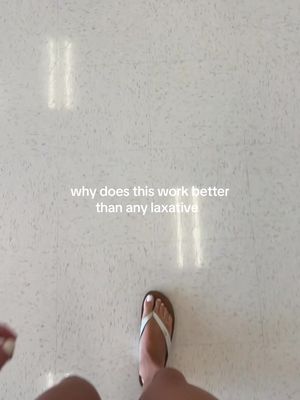 A first-person perspective shot shows a person's feet in a white-floored space, wearing a white and brown sandal while standing. Text overlayed on the image asks, 'why does this work better than any laxative'.