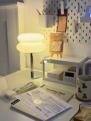 The cover image shows a well-lit desk setup with a retro-style lamp in the center, setting a cozy ambiance. In the background, a pegboard displays various items. In the foreground, a notebook and a book titled "Healthy diet" are visible, along with pencils and other study materials, suggesting a study or workspace.