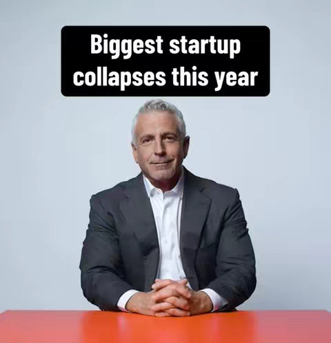 A man in a suit sits behind a red table. Above him is a black rectangle with the text 'Biggest startup collapses this year' in white. The background is a plain light blue.