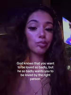 A young woman with long, wavy dark hair looks directly at the camera with a slightly pursed lip expression. The background is blurry with purple and dark tones. Text overlay appears in white font at the bottom, the text is related to love and faith.