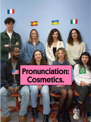 A group of people stand and sit in front of a blue wall. Behind them are various national flags, and in the front is a pink rectangle of text that reads "Pronunciation: Cosmetics."