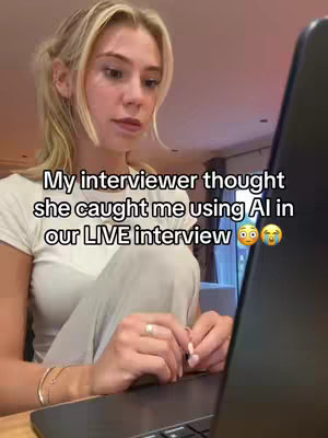 A young woman with blonde hair sits in front of a laptop, looking at the screen. Text overlays read: "My interviewer thought she caught me using AI in our LIVE interview 😲😭".