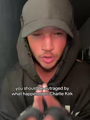 A person wearing a dark hoodie and cap looks directly at the camera and speaks. The text overlay reads, 'you should be outraged by what happened to Charlie Kirk'.