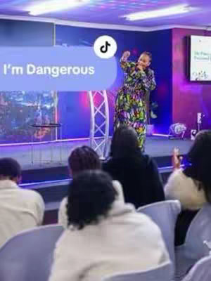 The cover image shows a woman on a stage during a church service. She is wearing a colorful, patterned dress and is gesturing with her hands. The background features the stage and the audience seating. In the middle there is a text bubble with the words I'm Dangerous displayed on it, and a tiktok symbol.