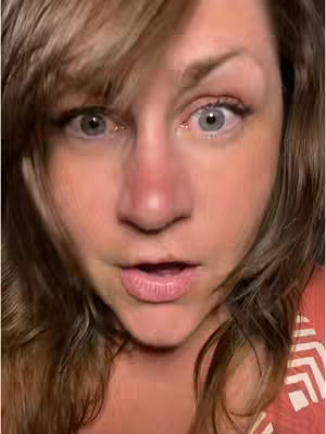 A close-up shot of a woman's face with wide eyes, a slightly open mouth, and a surprised expression. Her hair is brown and tousled, framing her face. She's wearing a patterned orange top. The lighting appears natural and the overall composition is centered on her face.