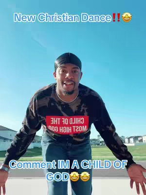 A man with a durag and a long-sleeved shirt with a design that says "CHILD OF GOD" in a red box stands facing the camera on a sunny day, with the sky in the background.