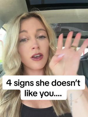 A woman with blonde hair is looking at the camera while holding up a hand with her fingers spread. Below her is a white banner with black text.