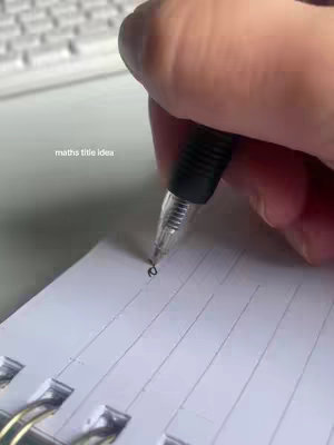 The cover image shows a hand holding a pen and writing on a white spiral notebook. The focus is on the pen's nib as it makes a small mark. The background includes a portion of a keyboard.