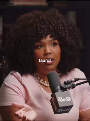 A woman with dark, curly hair is centered in a close-up shot, appearing to speak into a microphone with the word 'taurus' overlaid on top of her face, giving the astrological context.