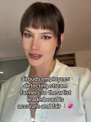 A woman with dark hair and bangs is centered in the frame. She wears a cream-colored top. Text overlayed on image.