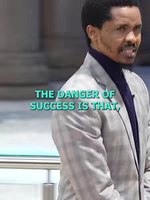The image shows a man in a grey suit, purple turtleneck, speaking in front of a blurred background. Text overlayed at the bottom states 'THE DANGER OF SUCCESS IS THAT'.
