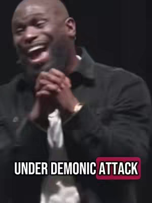 A man with a bald head and a beard is shown from the chest up, looking upwards with an open mouth and a slightly concerned expression. The text overlay reads "UNDER DEMONIC ATTACK" in white, placed over a partly red background.