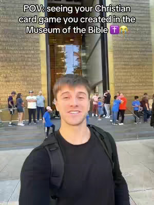 A selfie-style shot with a man in the foreground at the Museum of the Bible. The man is smiling broadly. Behind him is the museum facade with people walking around.