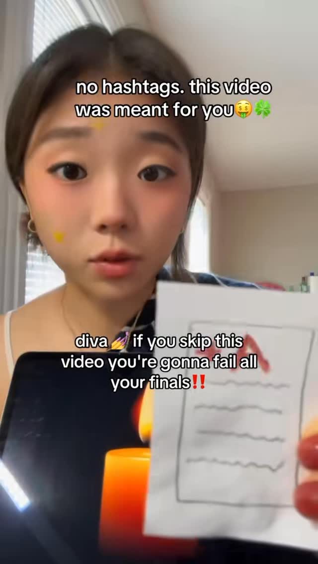 A young woman with pink blush and a yellow dot on her cheek looks towards the viewer. Text overlays include a warning about skipping the video. She holds a sheet of paper with a large red "A" grade marked on it. The background includes a room setting with warm light from a candle and some objects in the bottom right corner.